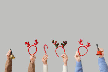 Female hands holding Christmas reindeer horns headbands with bells and candy cane on white background