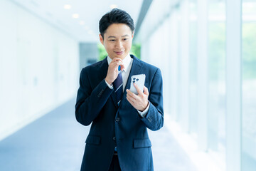 オフィスの廊下でスマホを操作するビジネスマン　