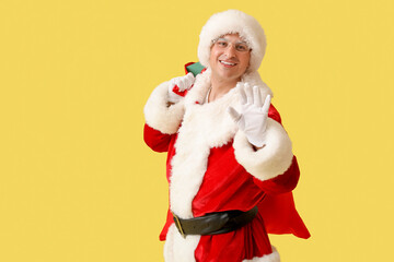 Young Santa Claus with bag of gifts on yellow background