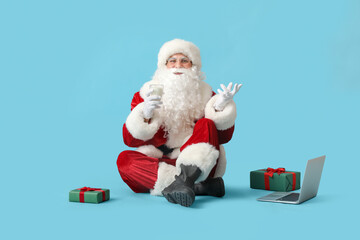 Santa Claus with glass of milk sitting on blue background