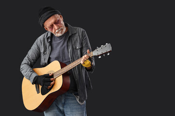 Obraz premium Mature homeless man playing guitar on dark background