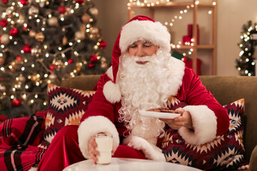 Santa Claus taking cookies and glass of milk from table at home on Christmas eve
