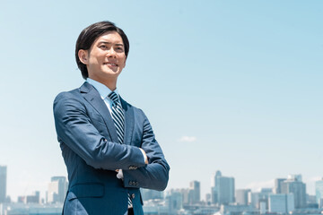 青空の中で腕組みする笑顔の若いアジア人ビジネスマン
