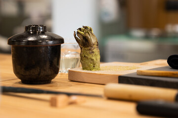 Fresh wasabi root on a wooden grater, accompanied by kitchen utensils in a Japanese culinary setting, highlighting traditional preparation
