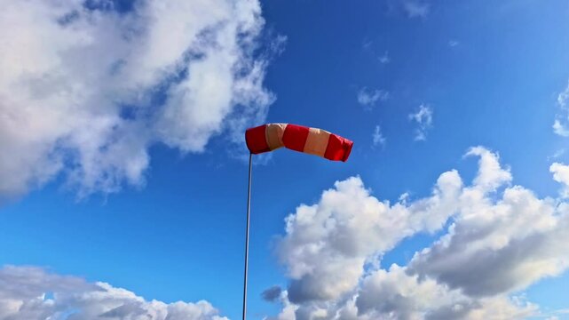 leicht im Wind wehende rot-wei&szlig;er Windsack vor blauem leicht bew&ouml;lkten blauem Himmel, Windrichtung, Windgeschwindigkeit, Wetter, Wetterbericht, Luftfahrt, Windrichtungsmesser