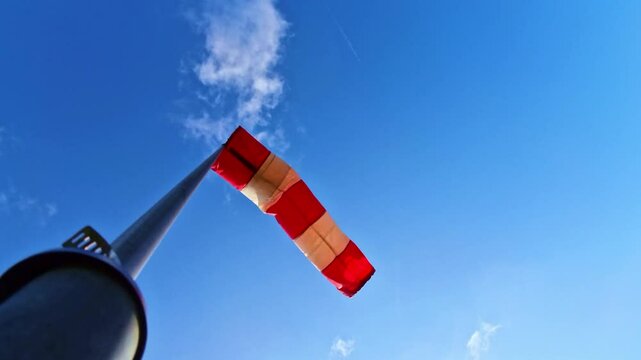 leicht im Wind wehende rot-wei&szlig;er Windsack vor blauem leicht bew&ouml;lkten blauem Himmel, Windrichtung, Windgeschwindigkeit, Wetter, Wetterbericht, Luftfahrt, Windrichtungsmesser