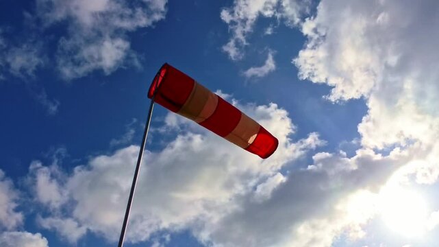 leicht im Wind wehende rot-wei&szlig;er Windsack vor blauem leicht bew&ouml;lkten blauem Himmel, Windrichtung, Windgeschwindigkeit, Wetter, Wetterbericht, Luftfahrt, Windrichtungsmesser