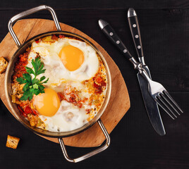 Delicious fried eggs with vegetables in pan with croutons on dark wooden table