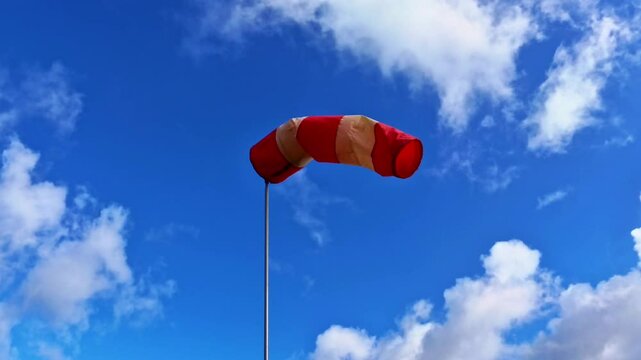 leicht im Wind wehende rot-wei&szlig;er Windsack vor blauem leicht bew&ouml;lkten blauem Himmel, Windrichtung, Windgeschwindigkeit, Wetter, Wetterbericht, Luftfahrt, Windrichtungsmesser
