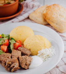 Traditional romanian food with polenta, pork stew, sour cream, cheese and salad on white wooden table