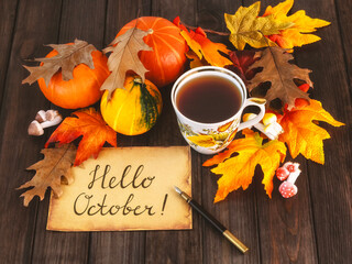 A sheet of paper with the inscription hello October, a vintage pen, a cup of tea, pumpkins, autumn leaves. Hello October concept