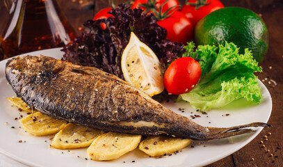Grilled fish with potatoes and vegetables on white plate being served on wooden table