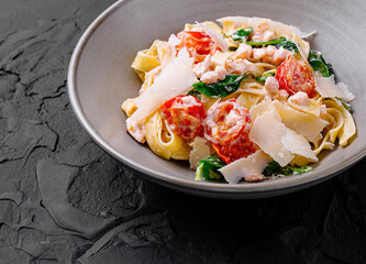 Pasta fettuccine with shrimps, spinach, cherry tomatoes and parmesan cheese on black background