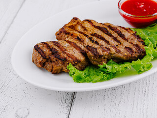 Grilled steak lying on fresh lettuce with tomato sauce on white plate