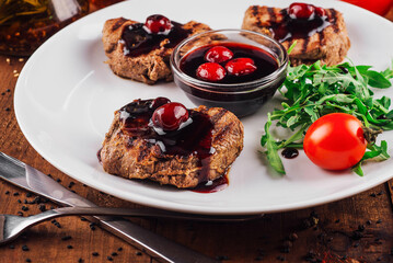 Grilled beef medallions with cherry sauce on white plate