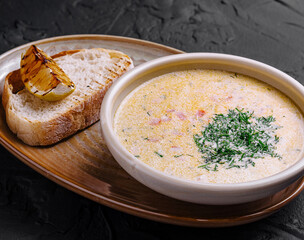 Creamy fish soup served in bowl with bread and grilled lemon on dark background
