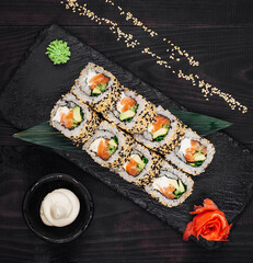 Sushi rolls set served on black stone plate on dark wooden table