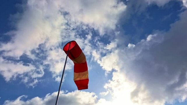 leicht im Wind wehende rot-wei&szlig;er Windsack vor blauem leicht bew&ouml;lkten blauem Himmel, Windrichtung, Windgeschwindigkeit, Wetter, Wetterbericht, Luftfahrt, Windrichtungsmesser