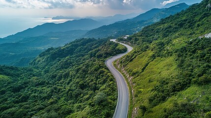 Fototapeta premium Breathtaking Mountain Landscape from Above: A Wide Road Winding Upward Through Lush Greenery and Rocky Terrain. This Scenic View Captures the Majesty of Nature, Showcasing Rolling Hills, Clear Skies, 