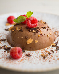 Dark chocolate flan with almonds. Decorated with cocoa powder and raspberries.