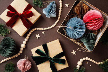 Christmas holiday decor with gift boxes, Nordic paper decorations, wooden beads, and pine branches on a brown background. Flat lay, top view.
