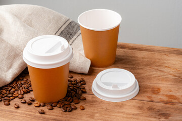 Disposable coffee cups placed on a wooden board with scattered coffee beans and a newspaper