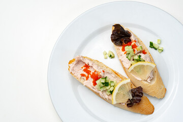 Tasty open-faced sandwiches with tuna spread, topped with fresh vegetables and lemon slices on a white plate