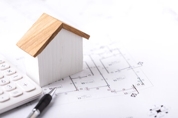 Concept of budgeting for home construction, with a house model, calculator, and construction plans placed on a table, symbolizing financial planning for building a home