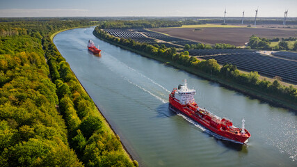 Tanker transporting fossil fuels along waterway, sailing past canal bordered by solar farm....