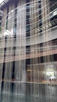 Cascading waterfall feature at one of modern contemporary hgih rise building. Modern architecture to incorporate water elements, using thread and wire to drip water. Green design, waterfall in buildin
