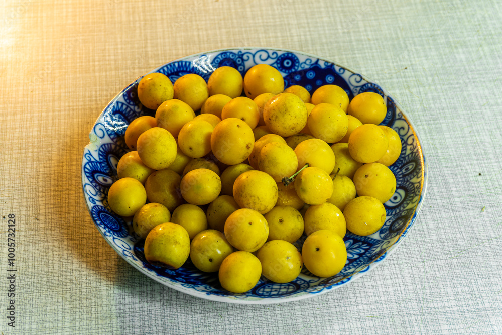 Wall mural heap of yellow tkemali fruits on plate with blue pattern on light table. prunus cerasifera, cherry p