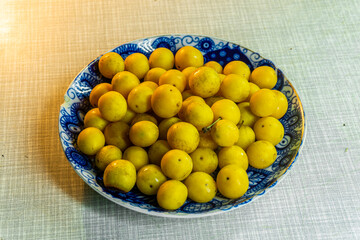 Heap of yellow tkemali fruits on plate with blue pattern on light table. Prunus cerasifera, cherry plum, myrobalan plum