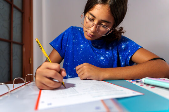 Young Girl Focused on Homework, Writing in Notebook at Study Desk