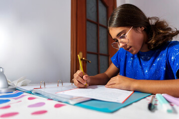 Young Girl Focused on Homework, Writing in Notebook at Study Desk