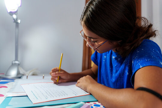 Focused Girl Studying and Writing in Notebook with Pencil at Home Desk