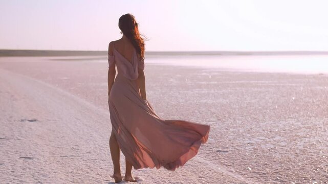 Woman in Flowing Dress Standing on Pink Salt Lake at Sunset