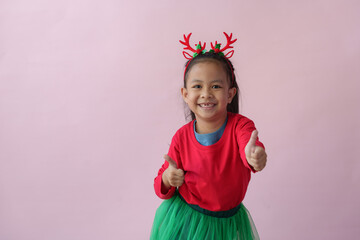 Adorable little Asian girl with Christmas tree headband, antlers showing various poses, standing, smiling, laughing, having fun in various poses, pink background. Holiday concept annual festival.