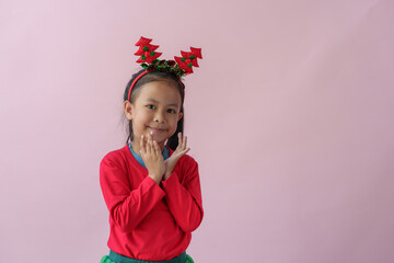 Adorable little Asian girl with Christmas tree headband, antlers showing various poses, standing, smiling, laughing, having fun in various poses, pink background. Holiday concept annual festival.