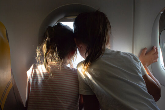Two excited girls looking out the airplane window during their first vacation flight. Travel, tourism and children.