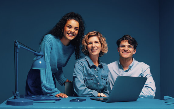 Diverse group of co-workers posing in a studio shot smiling with laptop and smartphone
