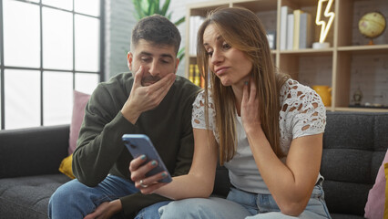 A concerned couple examines a smartphone together in a modern living room, reflecting relationship dynamics.