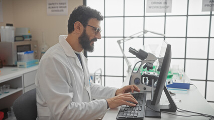 Mature bearded man in lab coat working at computer in modern laboratory setting.