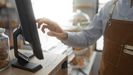 Young man working in a bakery shop, focused on the cash register touchscreen