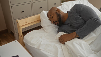 Handsome young african american man with a beard sleeping peacefully in bed in a cozy bedroom