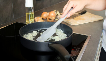 Close up a female hand stirring raw minced onions in a pan with a spatula, blurry background with onions and oil spray