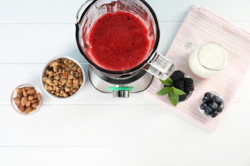 Blender with mixture of ingredients and other fresh products on white wooden table, top view