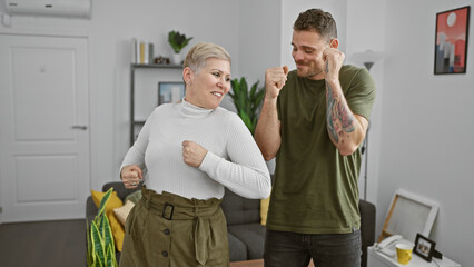 A smiling woman and man playfully fist bump in a modern living room, expressing friendship or partnership.