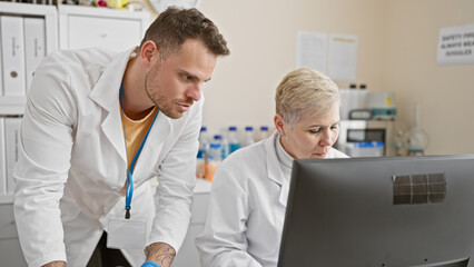 Obraz premium A man and woman, dressed in lab coats, intently analyze data on a computer screen in a modern laboratory setup.