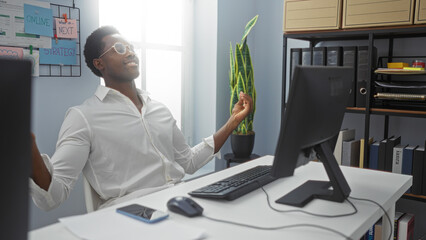 Handsome young african american man relaxing in an office with computer indoor showcasing a calm...