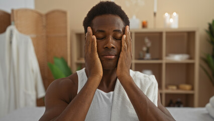 Young man enjoying a relaxing moment at a serene spa, with eyes closed and hands on face, towel...